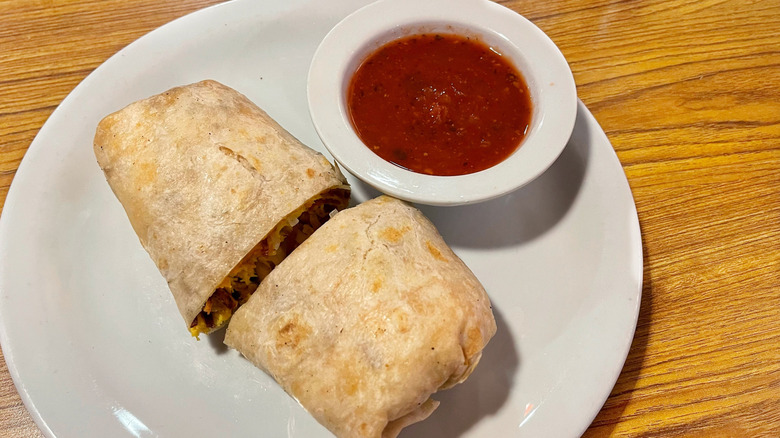The Grand Slam burrito on a plate, cut in half, served with a bowl of salsa
