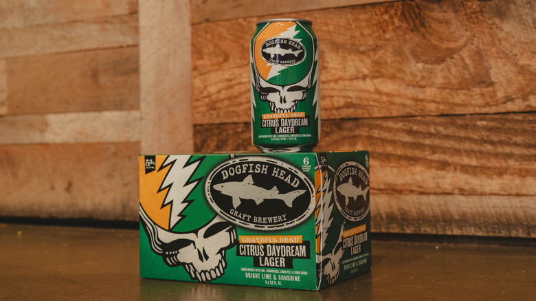 a can sits atop a case of Dogfish Head Grateful Dead Citrus Daydream Lager on floor in front of wooden wall