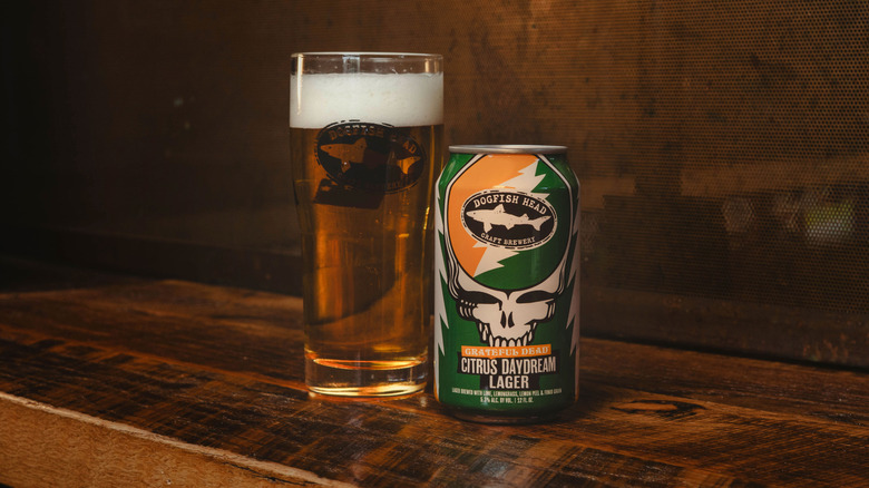 Dogfish Head Grateful Dead Citrus Daydream Lager can next to the beer poured into a glass on wooden surface
