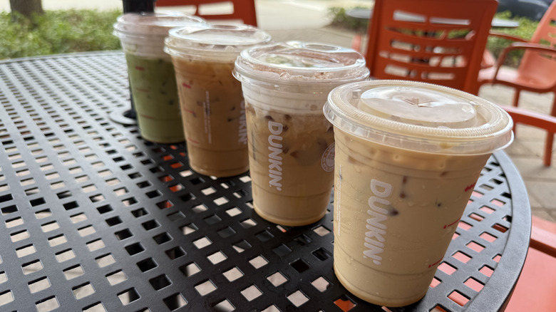 Four Dunkin' tiramisu cold beverages in takeout cups with lids on a metal table