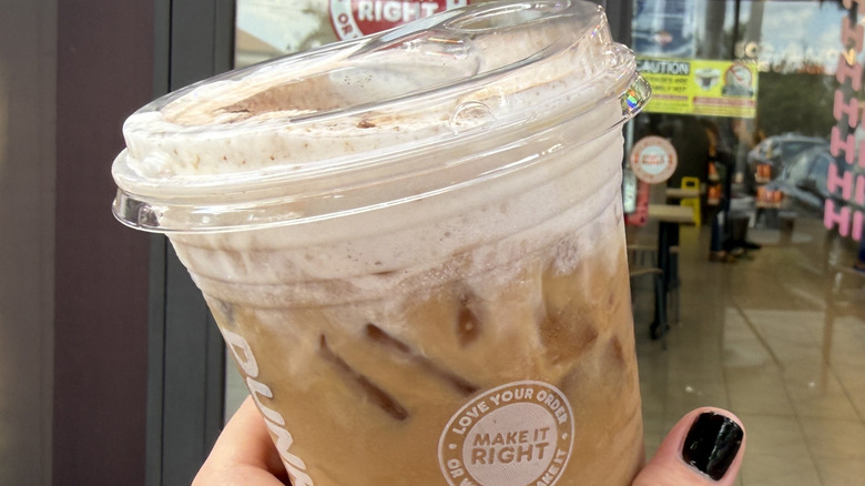 Hand holding a Dunkin' Tiramisu Cloud Latte in front of the store window