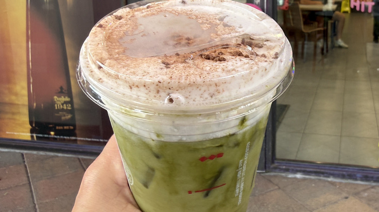 Hand holding a Dunkin' Tiramisu Marshmallow Matcha in front of the store window