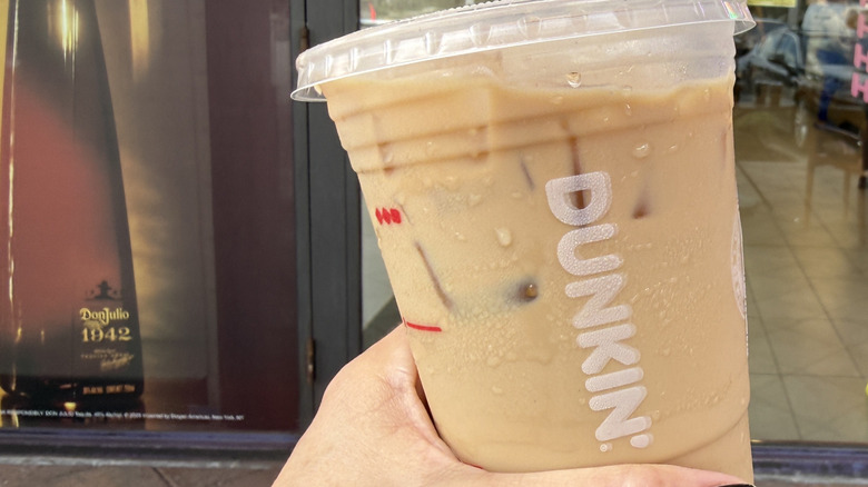 Hand holding a Dunkin' Tiramisu Protein Latte in front of the store window