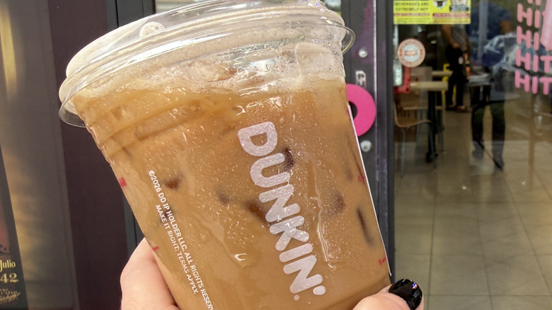 Hand holding a Dunkin' Tiramisu Shakin' Espresso in front of the store window