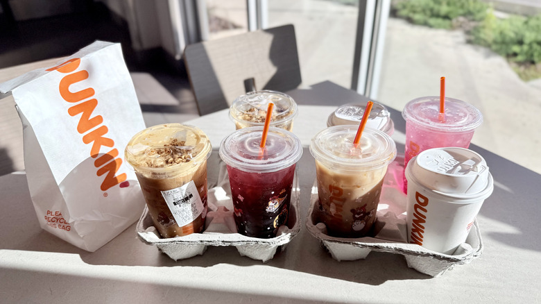 Seven drinks in containers on the table next to Dunkin' bag