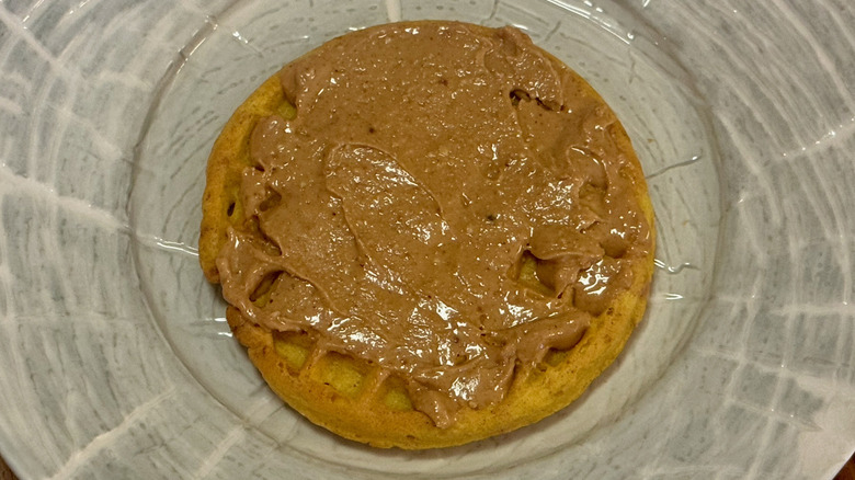 A toasted waffle with peanut butter on a white ceramic plate