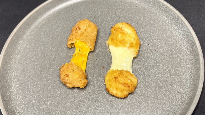 two cheese curds pulled apart on plate with darker cheese stretching on left and lighter cheese on right