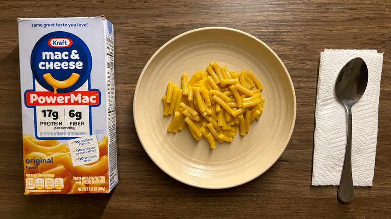 Kraft PowerMac box and macaroni and cheese on a plate with a silver spoon on a napkin on a wooden table