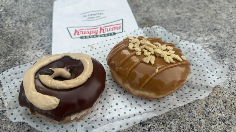 Two doughnuts resting on serving paper with Krispy Kreme bag in background