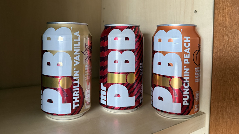 Three flavors of Mr. Pibb sit in a cabinet