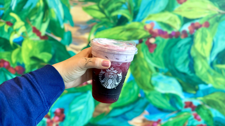 Hand holding Starbucks' Hannah Montana Popstar Refresher in front of a painting