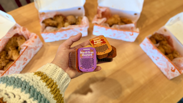 hand holding sauces in front of chicken wings in boxes