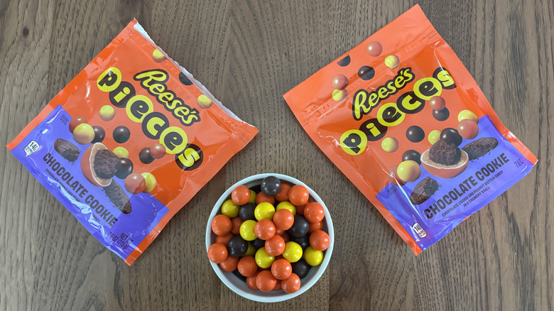 Bowl of new Reese's Pieces with chocolate cookie with bags of candy laid flat
