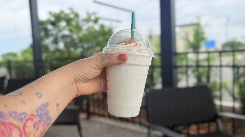 Hand holding an Horchata Crème Frappuccino from Starbucks in a plastic to-go cup with a green straw in it
