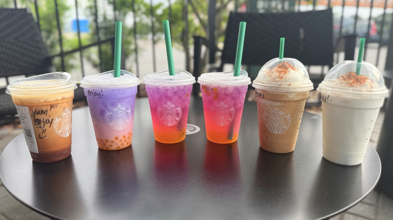 Six drinks in plastic to-go cups from Starbucks lined up on a black table
