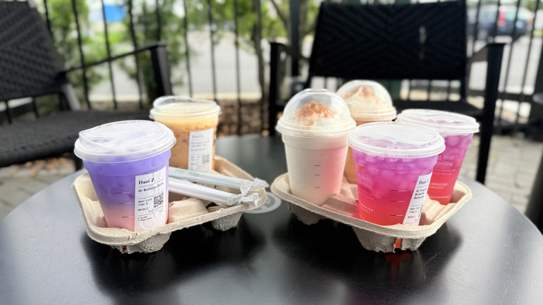 Six Starbucks drinks in plastic to-go cups in drink carriers resting on a black table