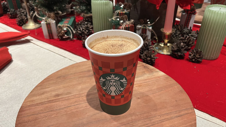 A Starbucks Eggnog Latte in holiday cup with holiday decorations in the background