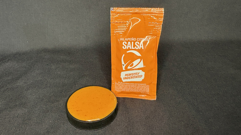 orange Taco Bell sauce packet standing next to cup of sauce