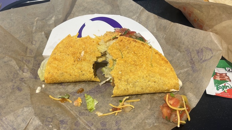 A broken Tajín taco sits on a tray on table