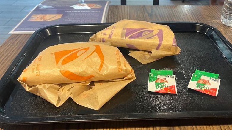 Two wrapped Taco Bell tacos on tray with packets of Tajín seasoning