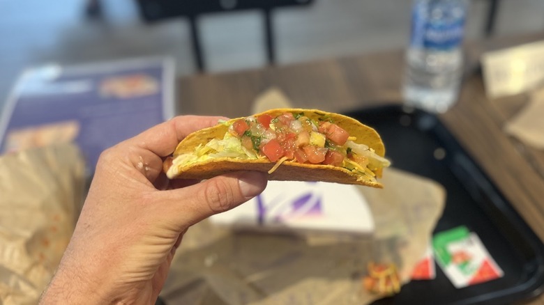 A hand holds a Tajín Taco from Taco Bell above tray on table