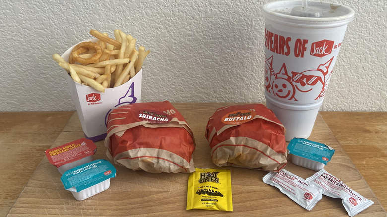 Both sandwiches wrapped surrounded by fries, a drink, and sauce packets