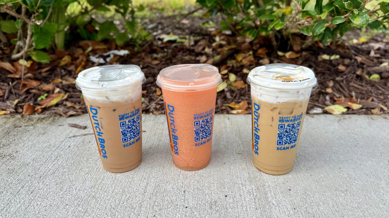 Three Dutch Bros iced drinks in to-go cups sitting on sidewalk