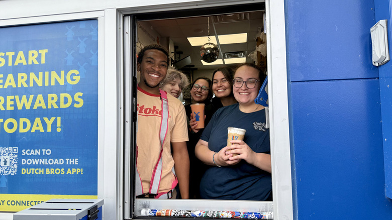 Smiling Dutch Bros staff at drive-thru window holding drinks