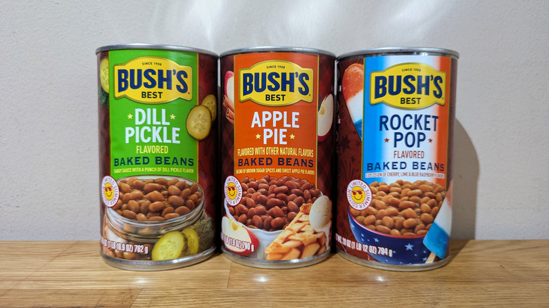 Three Bush's Best bean cans labeled Dill Pickle, Apple Pie,  and Rocket Pop