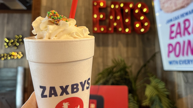 Zaxby's Nerds Strawberry Milkshake in styrofoam takeout cup held up in front of wall inside a Zaxby's restaurant