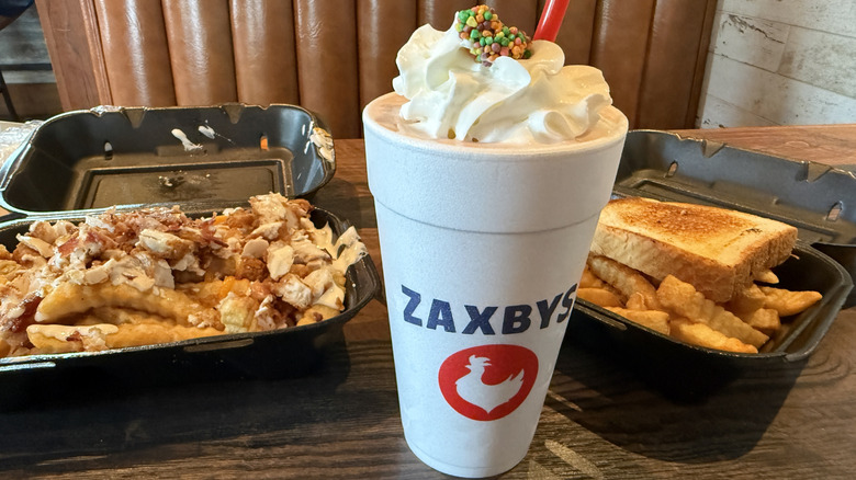 Zaxbys Nerds strawberry milkshake topped with whipped cream and Nerds candy with order of fries on table inside restaurant