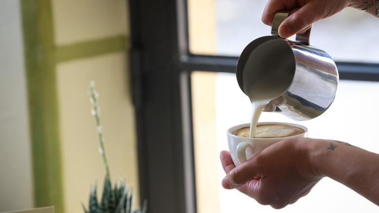 Person pouring milk into cappuccino