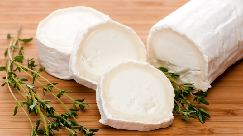 Sliced pieces of goat cheese beside fresh thyme on a wooden surface