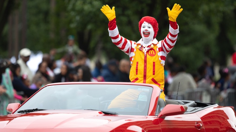 Ronald McDonald waving to a crowd during a motorcade.