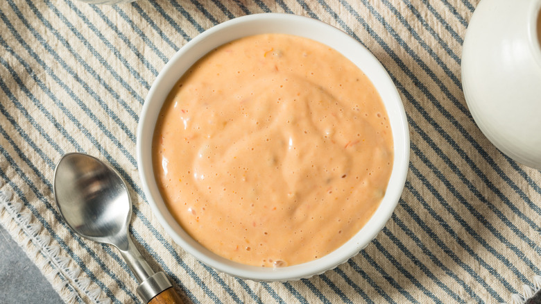 Russian dressing in bowl with a spoon on striped linens