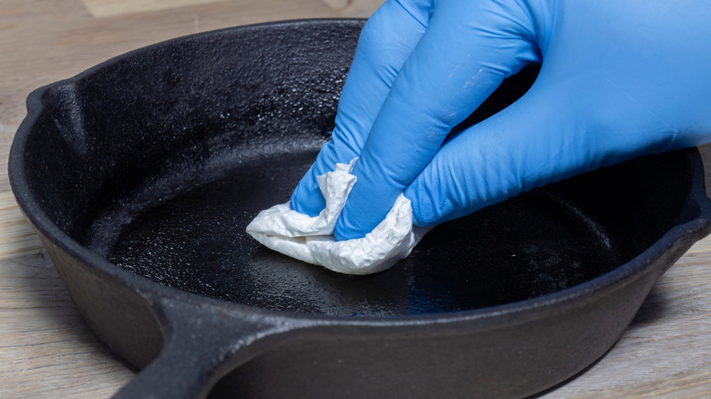 A cast iron pan being seasoned with oil by a person wearing blue gloves