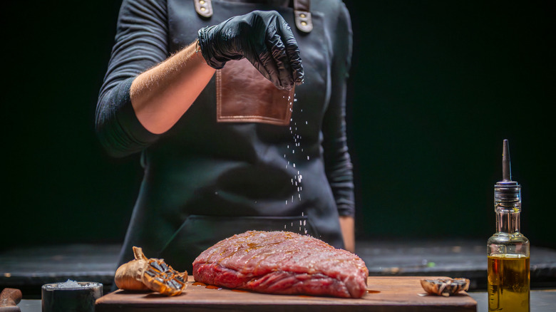Chef seasoning a large piece of raw beef with salt.