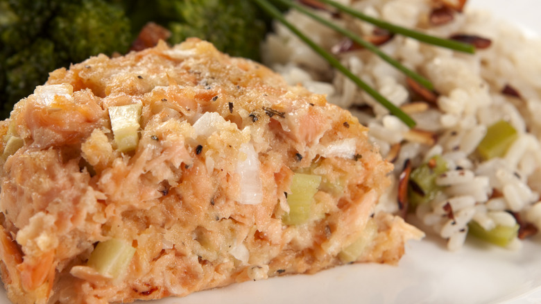 A closeup of a baked salmon meatloaf on a plate with rice pilaf and broccoli