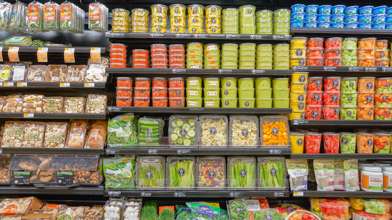 Refrigerated salsa, guacamole, and cut up fruit and vegetables on display on grocery store refrigerated shelf.
