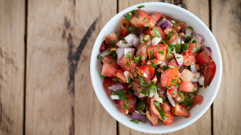 White bowl of fresh pico de gallo on wooden table.