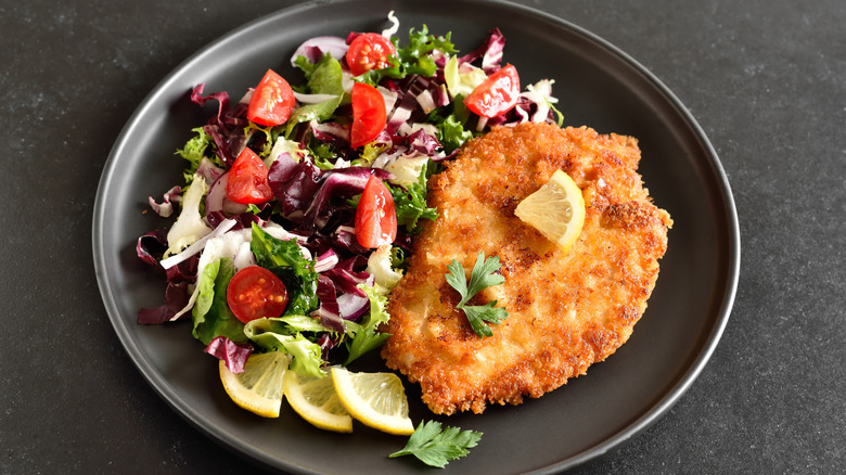 Crispy chicken cutlet alongside a green salad on a plate