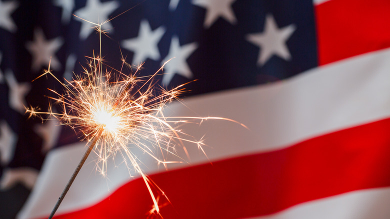 An American flag with a sparkler in the foreground.