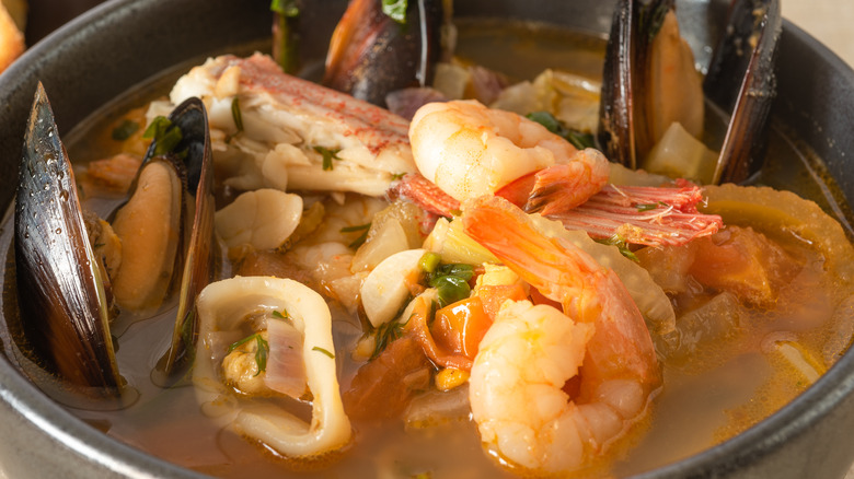 A closeup of cioppino with mussels, shrimp, fish, and other seafood in a broth