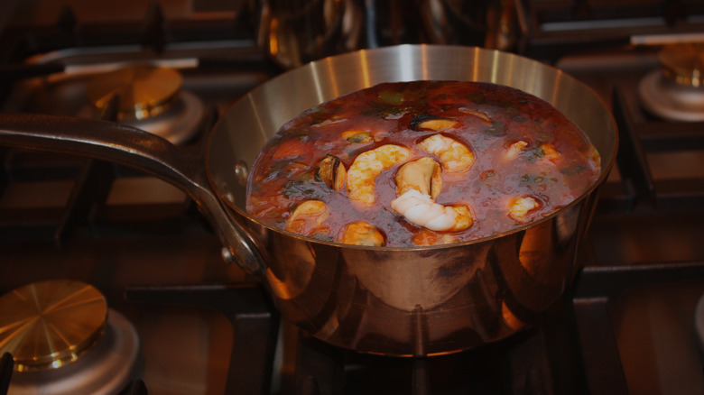 A copper pot of cioppino simmering on a stove
