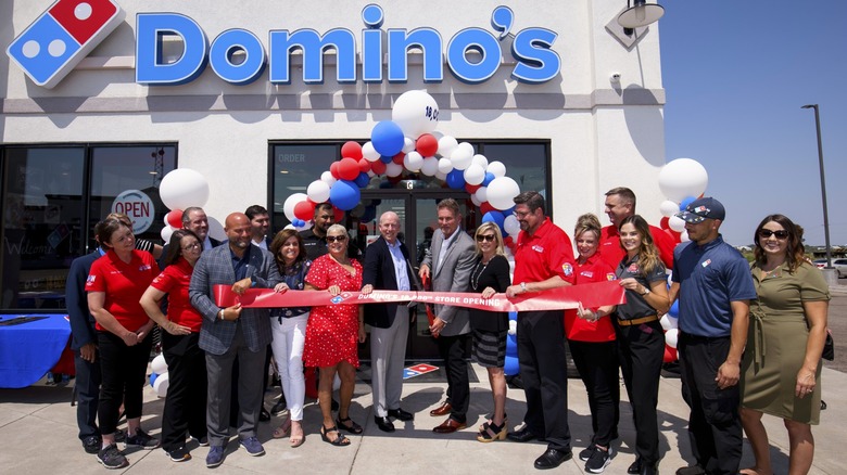 A Domino's franchise owner and others at ribbon-cutting ceremony in front of store