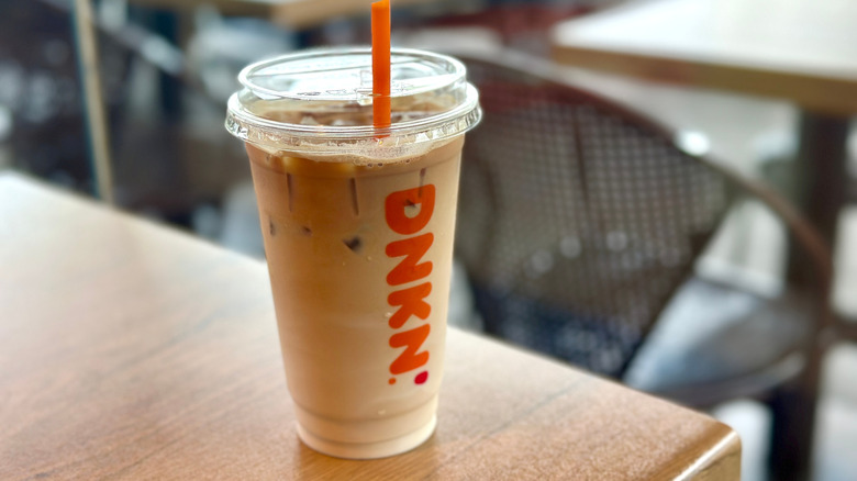 A plastic Dunkin' cup full of an iced latte on a wooden table