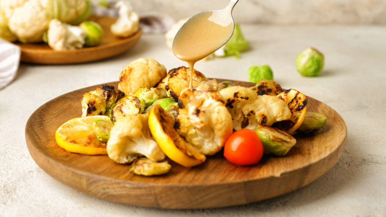Spooning creamy sauce or dressing over roasted cauliflower on a plate