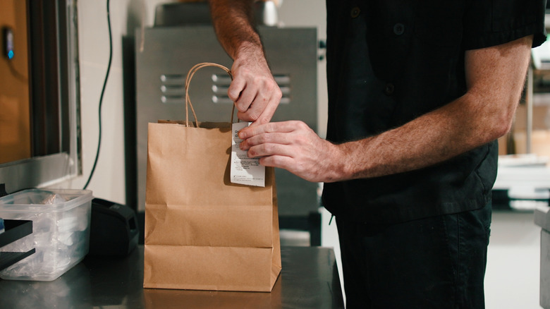 A chef preparing a takeout order by stapling the bag shut.