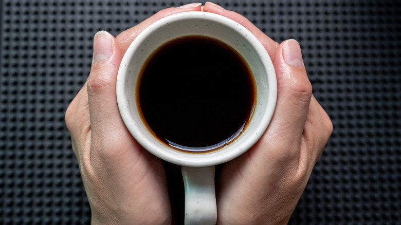 Someone holding a cup of black coffee with two hands