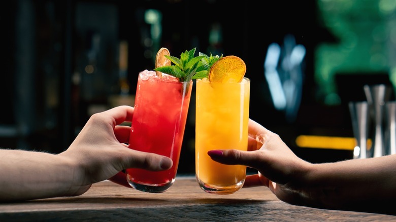 Two colorful cocktails being clinked together.